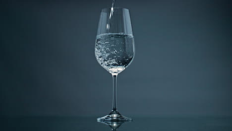 Reines-Wasser-Füllt-Glas-Vor-Dunklem-Hintergrund,-Nahaufnahme.-Blasen-Steigen-Transparent-Auf