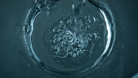 Draufsicht:-Wasser-Gießt-Transparente-Tasse,-Nahaufnahme.-Verschiedene-Luftblasen-Fließen