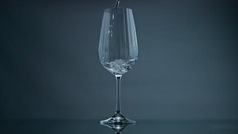 Wasser-Gießt-Weinglas-Auf-Dunklem-Hintergrund,-Nahaufnahme.-Klare-Flüssigkeit-Spritzt