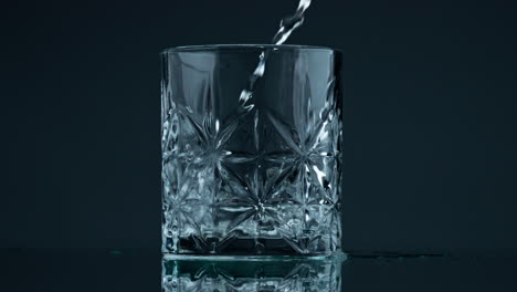 Gießen-Von-Wasser-Aus-Kristallglas-Auf-Dunklem-Hintergrund,-Nahaufnahme.-Flüssigkeitsstrom-Fällt