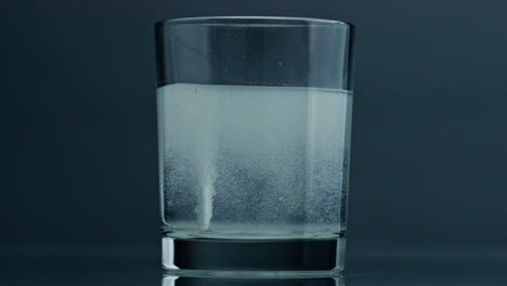 White-pill-dissolving-glass-at-dark-background-closeup.-Effervescent-tablet-flow