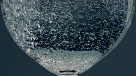 Closeup-bubbles-rising-glass-surface-at-dark-background.-Fresh-pure-beverage-in