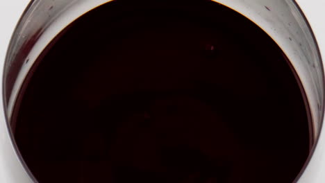 Rotweintropfen-Fallen-Aus-Glas,-Nahaufnahme.-Glatte,-Kreisförmige-Kräuselung-Der-Flüssigkeitsoberfläche