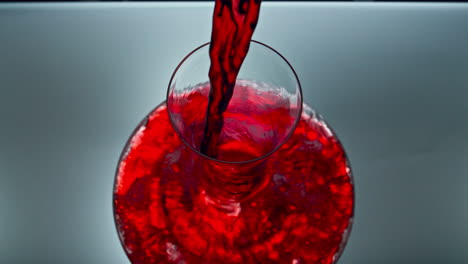 Closeup-pouring-red-wine-glass-bowl-indoors.-Alcoholic-liquid-filling-decanter