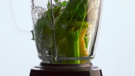 Vegetables-blender-poured-water-close-up.-Organic-veggies-fruits-herbs-in-mixer.