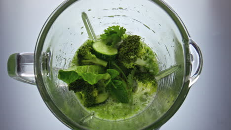 Blender-start-mixing-vegetable-fruits-herbs-close-up-top-view.-Vitamin-food.