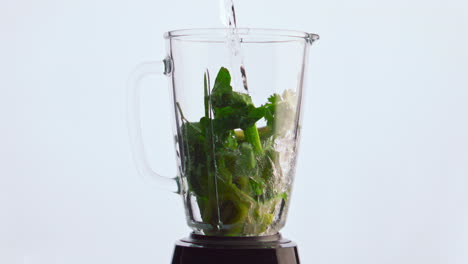 Fresh-vegetables-dropped-blender-pouring-with-water-close-up.-Veggies-in-mixer.