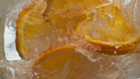 Orange-slices-falling-glass-liquid-closeup.-Making-fizzy-citrus-cocktail-in-cup.