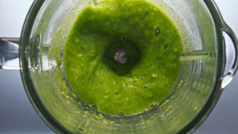 Top-view-green-smoothie-swirling-in-blender-bowl-close-up.-Organic-veggies-herbs