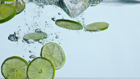 Closeup-lime-slices-underwater-on-white-background.-Citrus-falling-under-water.