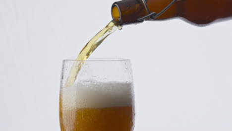 Nahaufnahme-Einer-Flasche-Bier,-Die-Auf-Weißem-Hintergrund-In-Ein-Glas-Gießt.-Lagergetränk-Fließt