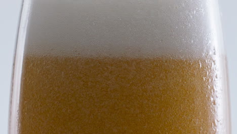 Weißer-Bierschaum-Sprudelt-Auf-Glas-Vor-Weißem-Hintergrund,-Nahaufnahme.-Wirbelnde-Blasen