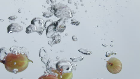 Fresh-gooseberry-falling-water-making-bubbles-at-white-background-close-up.
