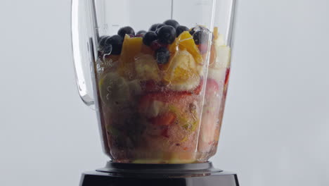 Electric-blender-blending-fruits-berries-with-water-for-natural-cocktail-closeup