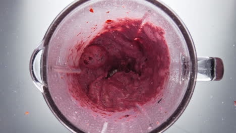 Tasty-red-berries-smoothie-mixing-in-blender-close-up-top-view.-Sweet-milkshake
