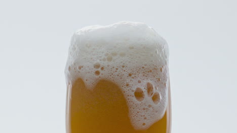 Bierschaum-Aus-Fließendem-Glas-Auf-Weißem-Hintergrund,-Nahaufnahme.-Sprudelndes-Alkoholisches-Getränk.