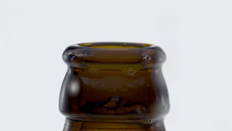 Beer-droplets-falling-bottle-neck-after-opening-at-white-background-close-up.