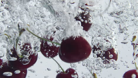 Ripe-cherries-falling-water-making-splashes-bubbles-at-white-background-close-up