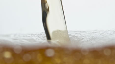 Closeup-beer-stream-pouring-on-bubbling-drink-surface-at-white-background.