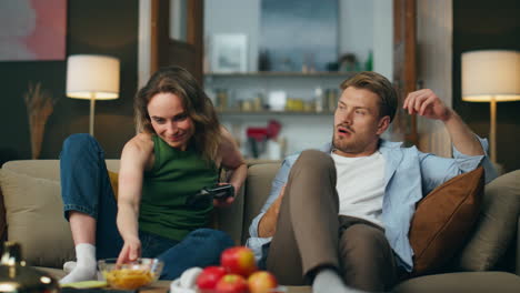 Smiling-woman-giving-snacks-to-man-at-sofa.-Loosing-guy-taking-remote-controller