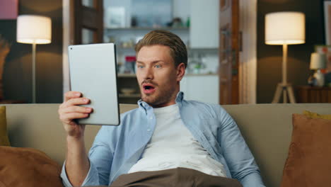 Surprised-man-reading-tablet-screen-at-house-closeup.-Wondering-guy-watching-tab