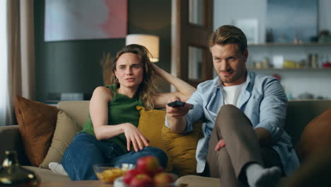 Relaxed-partners-chilling-sofa-watching-tv-evening.-Smiling-man-turning-channels