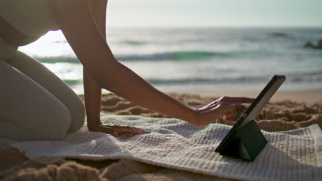 Girl-putting-tablet-yoga-mat-lying-sand-beach-close-up.-Woman-preparing-training