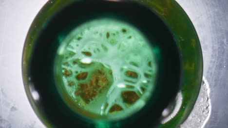 Cold-ale-overflowing-bottle-closeup.-Wheat-beer-making-foam-green-glassy-vessel