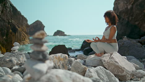 Girl-relaxing-sitting-lotus-pose-on-stone-Ursa-beach-vertical.-Woman-meditating
