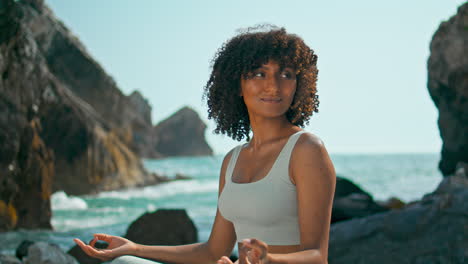 African-girl-meditating-lotus-position-on-rocky-shore-Ursa-beach-close-up