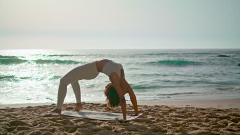 Woman-performing-bridge-pose-at-sunrise.-Girl-practicing-yoga-asana-on-beach.