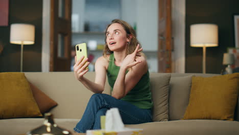 Flirting-girl-videocalling-cellphone-sofa.-Smiling-woman-gesturing-hands-talking