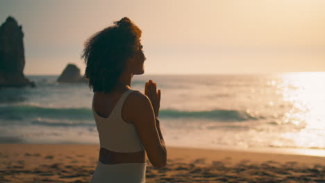 Back-view-woman-meditating-sitting-with-namaste-hands-in-front-sunrise-close-up.
