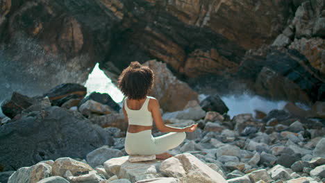 Back-view-girl-sitting-lotus-pose-in-front-cliff-of-Ursa-beach.-Woman-meditating