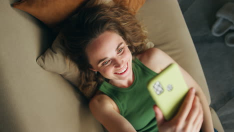 Happy-girl-waving-hand-speaking-smartphone-top-view.-Relaxed-woman-laying-couch