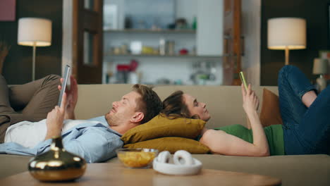 Entspanntes-Paar-Beim-Surfen-Auf-Dem-Sofa,-Frau-Simst-Telefon,-Mann-Liest-Tablet