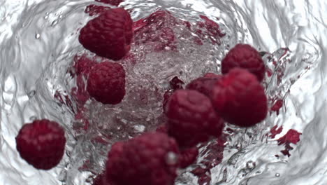 Berries-throwing-whirlpool-water-glassware-top-view.-Raspberries-moving-in-aqua