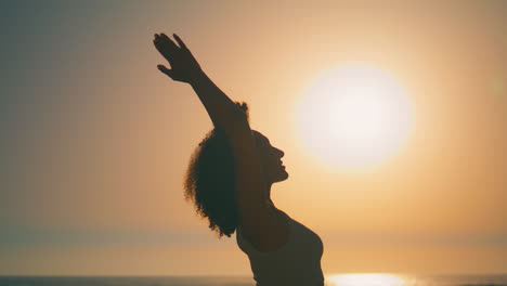 Silhouette-woman-raising-hands-to-sky-on-beach-sunrise-close-up.-Girl-meditation