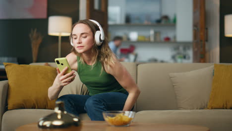 Earphones-woman-listening-music-laying-sofa-at-flat.-Relaxed-girl-sitting-couch