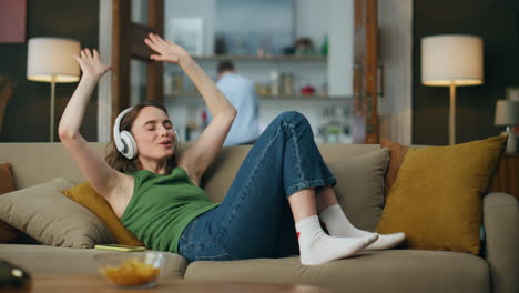 Headphones-woman-enjoying-music-laying-sofa-indoors.-Happy-girl-moving-hands