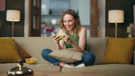 Excited-woman-laughing-smartphone-at-home-couch.-Happy-lady-playing-mobile-phone