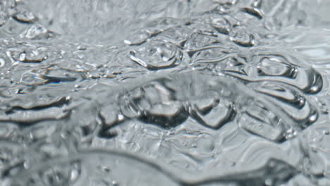 Nahaufnahme-Eines-Sprudelnden-Wasserglases-Aus-Eis.-Mineralwasserflüssigkeit,-Plätschernde-Textur-Des-Kelchs