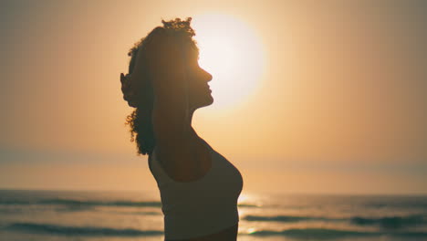 Sporty-girl-warming-body-in-front-sunrise-close-up.-Silhouette-athletic-woman.