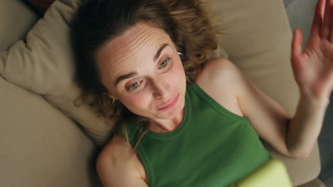 Smiling-woman-videocalling-telephone-laying-sofa-closeup.-Happy-girl-talking
