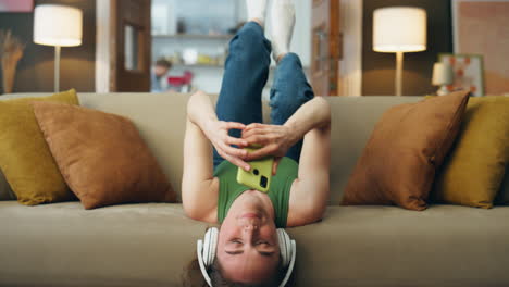 Headphones-girl-laying-sofa-listening-music-closeup.-Happy-woman-texting-phone