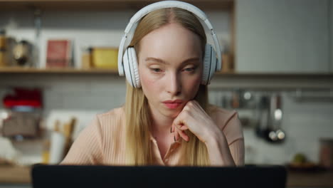Girl-freelancer-watching-training-video-in-headphones-sitting-kitchen-close-up.