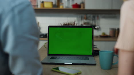 Couple-watching-green-screen-laptop-sitting-at-kitchen-table-with-coffee-closeup