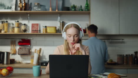 Woman-listening-training-course-sitting-on-kitchen-with-laptop-headphones