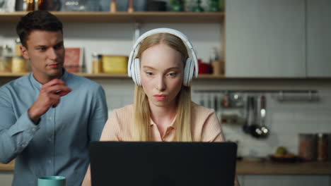 Business-woman-working-home-on-laptop-with-headset-man-trying-distract-closeup