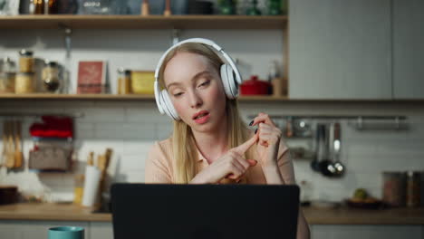 Woman-teacher-lecturing-online-sitting-at-kitchen-with-laptop-wearing-headphones